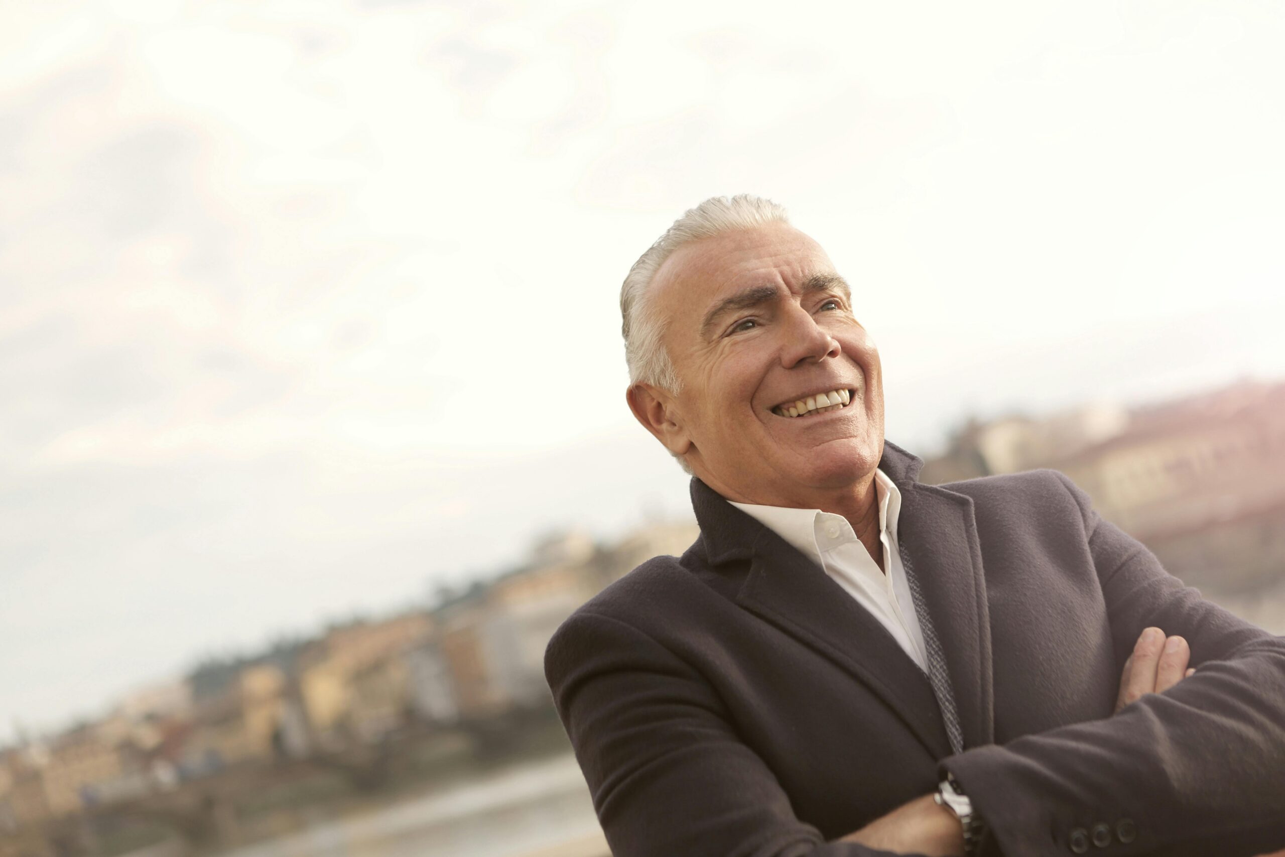 A senior man in business attire smiles confidently during a sunny outdoor setting.